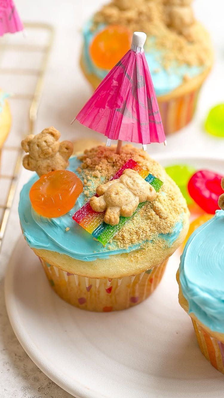 26 Beach Cake Ideas with Blue Ocean Frosting to Sailboats 2 Beach themed cupcake with blue ocean frosting, brown sugar sand, and a pink umbrella.