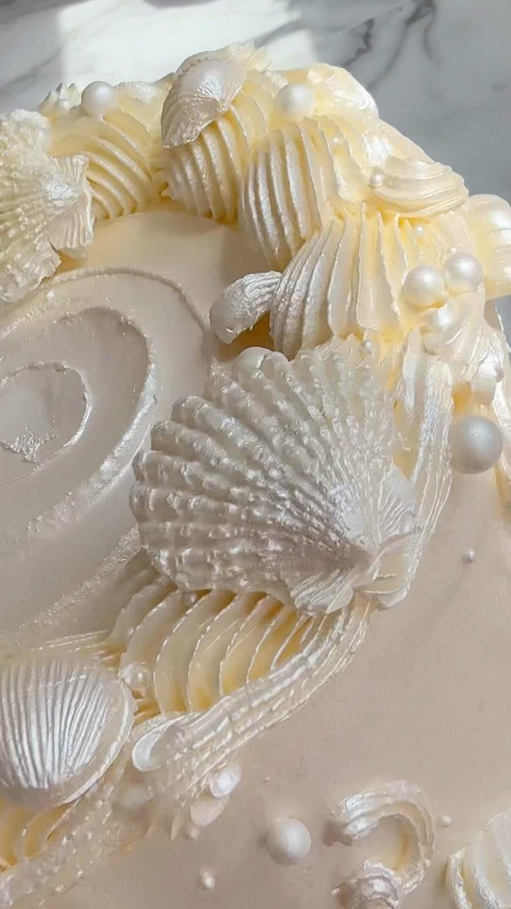 26 Beach Cake Ideas with Blue Ocean Frosting to Sailboats 25 White frosted cake with piped cream, edible pearls, and white chocolate seashells.