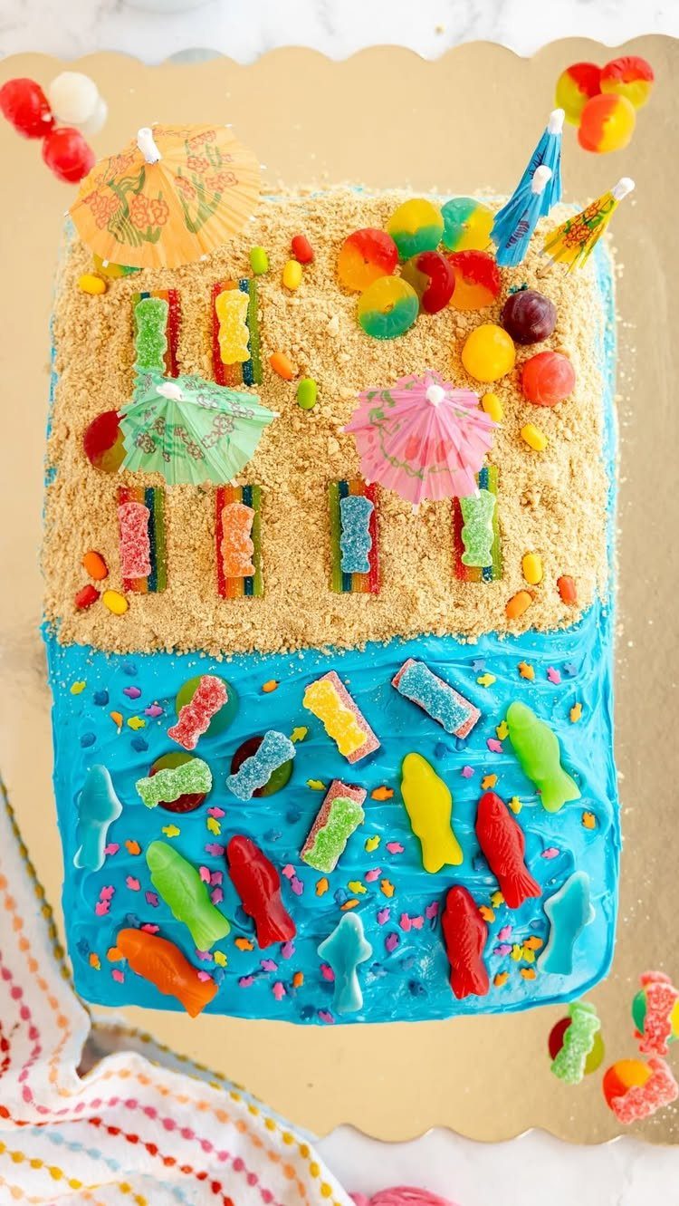 26 Beach Cake Ideas with Blue Ocean Frosting to Sailboats 17 Beach themed cake with sandy crumbs, blue frosting water, gummy fish and umbrellas.