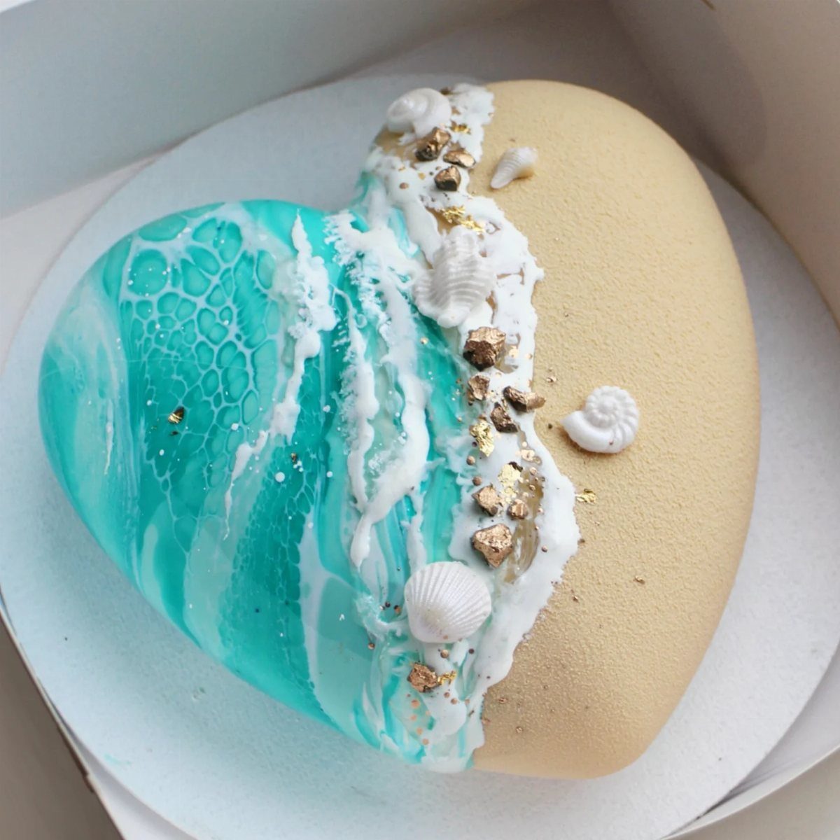 26 Beach Cake Ideas with Blue Ocean Frosting to Sailboats 8 Heart-shaped beach cake with teal marbled water, tan sand frosting, and small seashells.