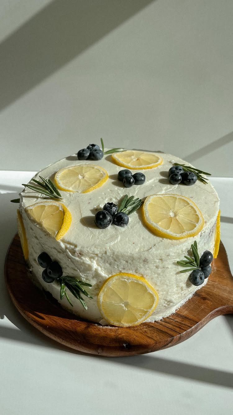 26 Beach Cake Ideas with Blue Ocean Frosting to Sailboats 3 White frosted cake decorated with fresh lemon slices, blueberries, and rosemary sprigs.