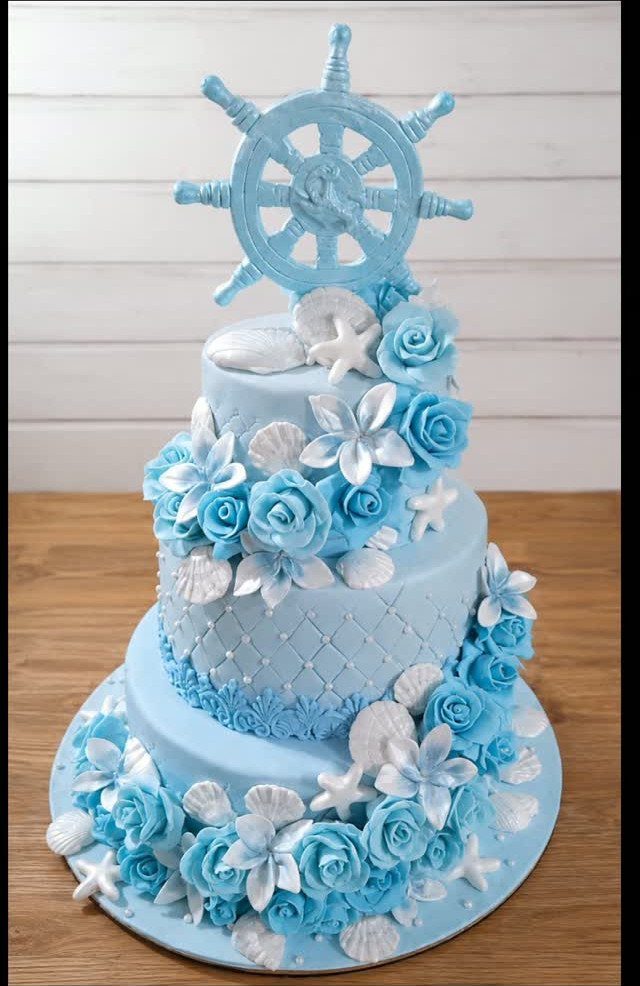 26 Beach Cake Ideas with Blue Ocean Frosting to Sailboats 16 Three-tiered blue beach cake with seashells, starfish, and a ship's wheel topper.