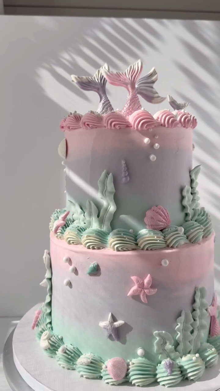 26 Beach Cake Ideas with Blue Ocean Frosting to Sailboats 9 Two-tiered pastel mermaid cake with frosting waves, seashells, and green frosting seaweed.