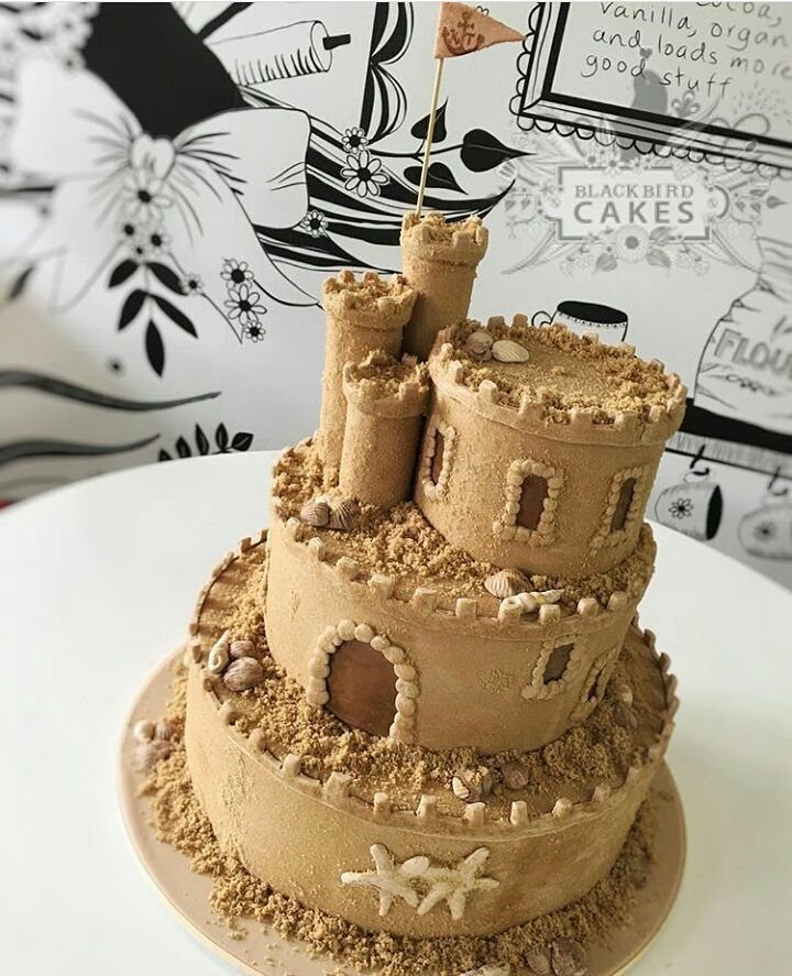 26 Beach Cake Ideas with Blue Ocean Frosting to Sailboats 13 Sandcastle themed cake with tan frosting, edible sand, and small seashells on a plate.