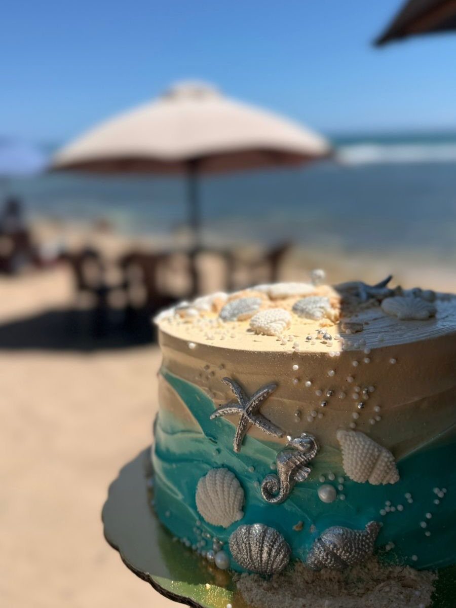 26 Beach Cake Ideas with Blue Ocean Frosting to Sailboats 19 Beach themed cake with blue frosting, edible sand, and seashells on a sunny beach.