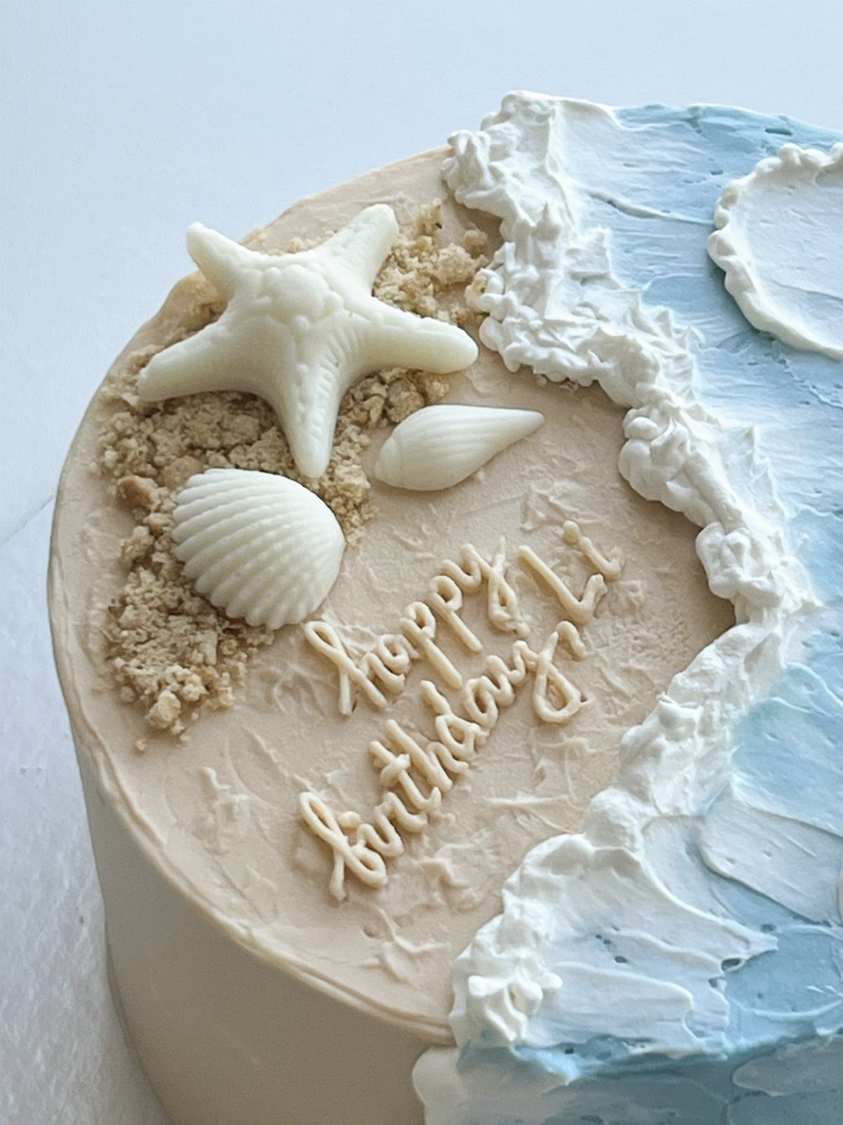 26 Beach Cake Ideas with Blue Ocean Frosting to Sailboats 7 Beach-themed birthday cake with blue frosting waves, white chocolate seashells, and a starfish.