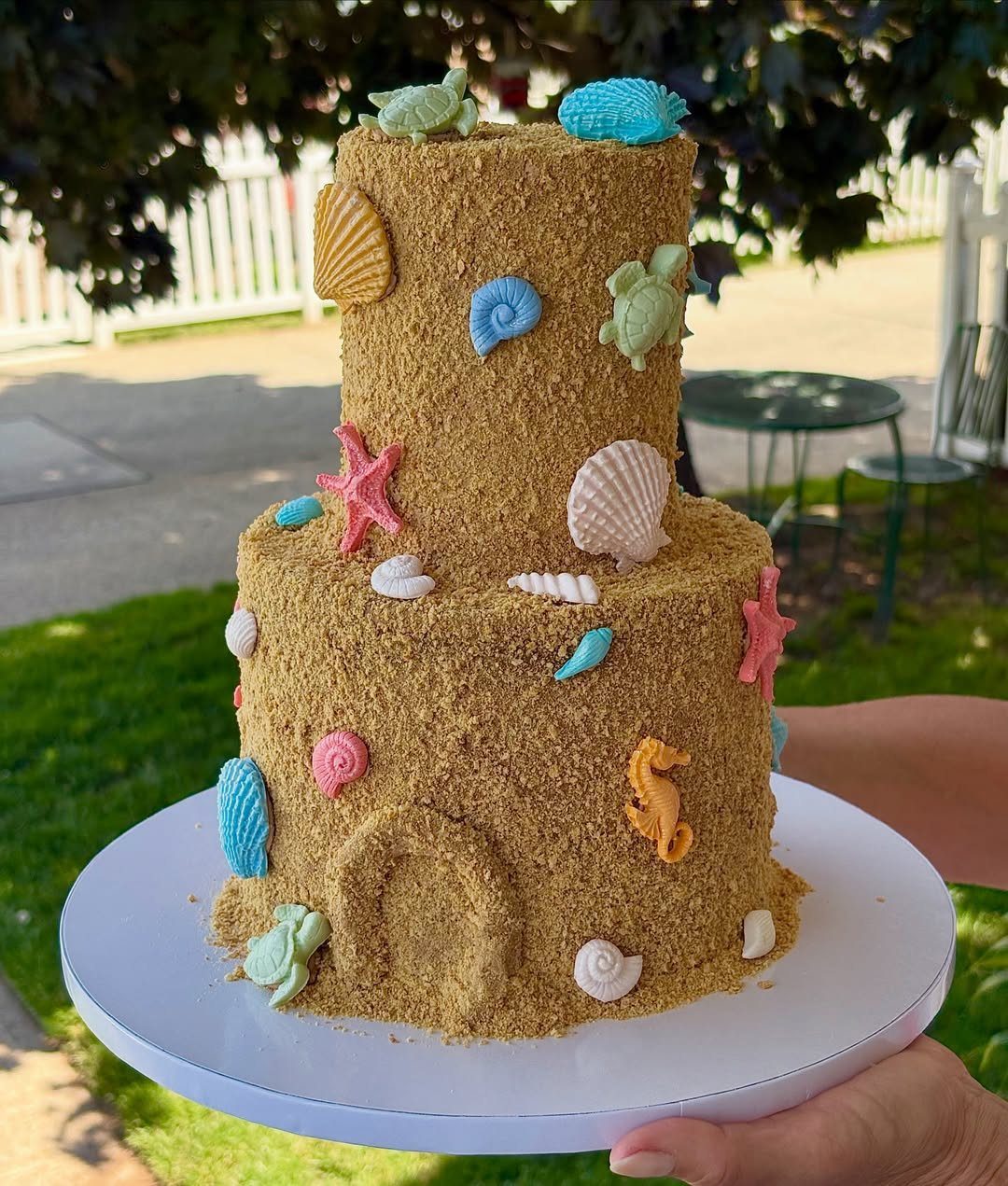 26 Beach Cake Ideas with Blue Ocean Frosting to Sailboats 5 Two-tiered sand-textured cake decorated with colorful edible seashells, starfish, and sea turtles.