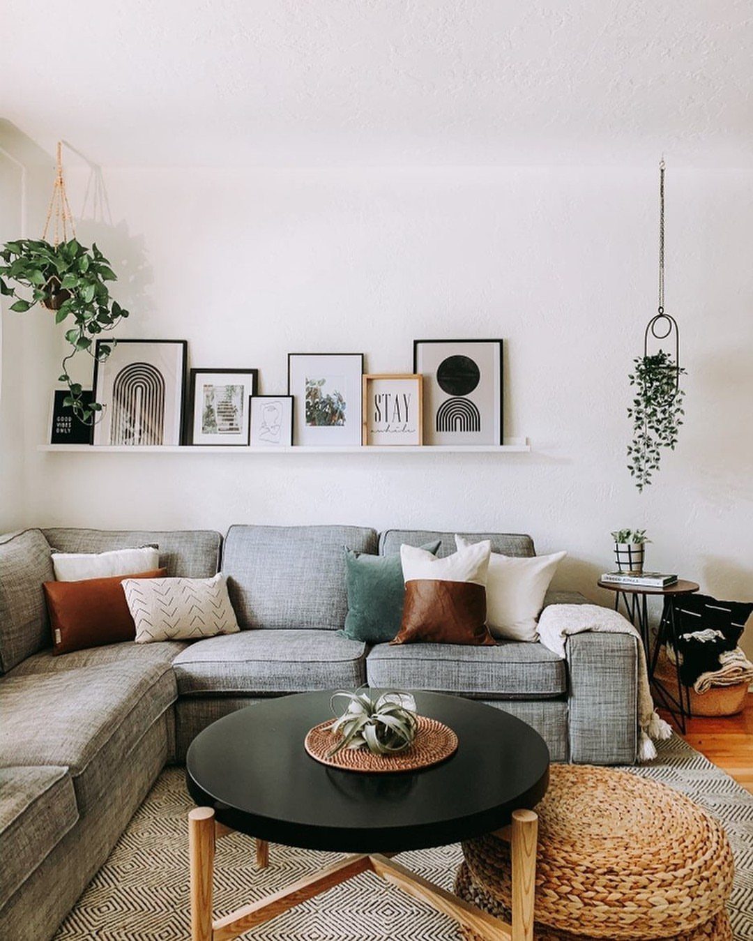White floating shelf with framed art mounted above a grey sectional sofa in a living room.