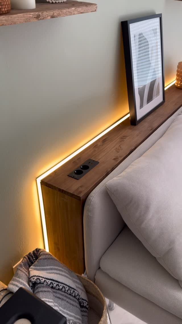 Wooden floating shelf with integrated lighting installed behind a light grey fabric sofa