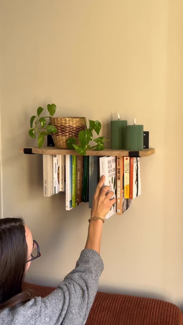 Wooden floating shelf with hanging books and plants mounted above a brown couch.