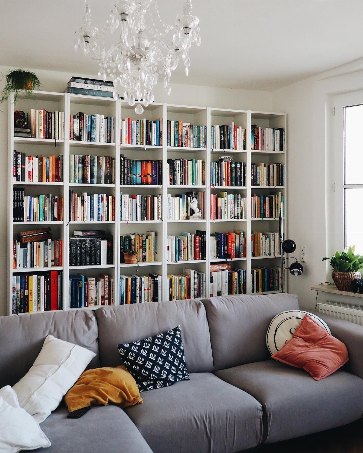 White grid bookshelf filled with books mounted on a wall above a grey couch.