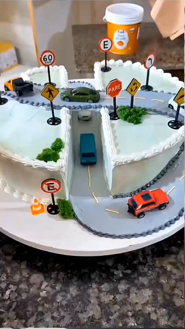 White frosted cake shaped like a highway with toy cars and road signs.