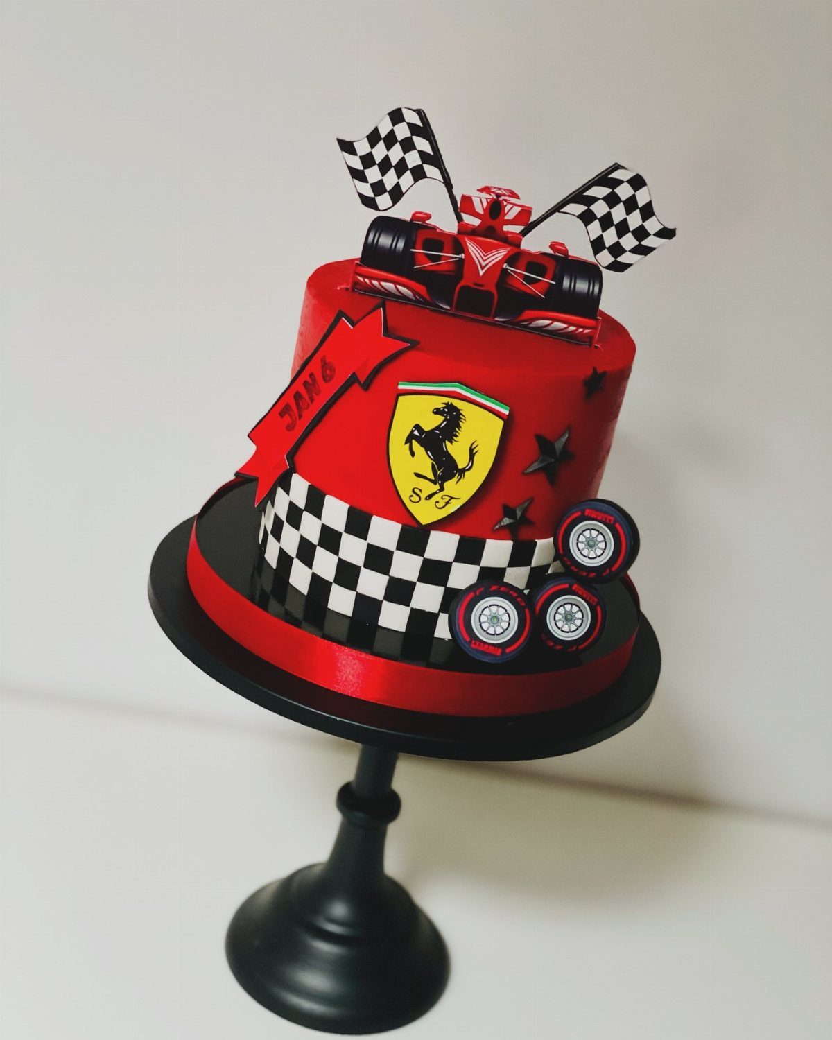 Red race car cake with checkered flags and Ferrari logo on black stand