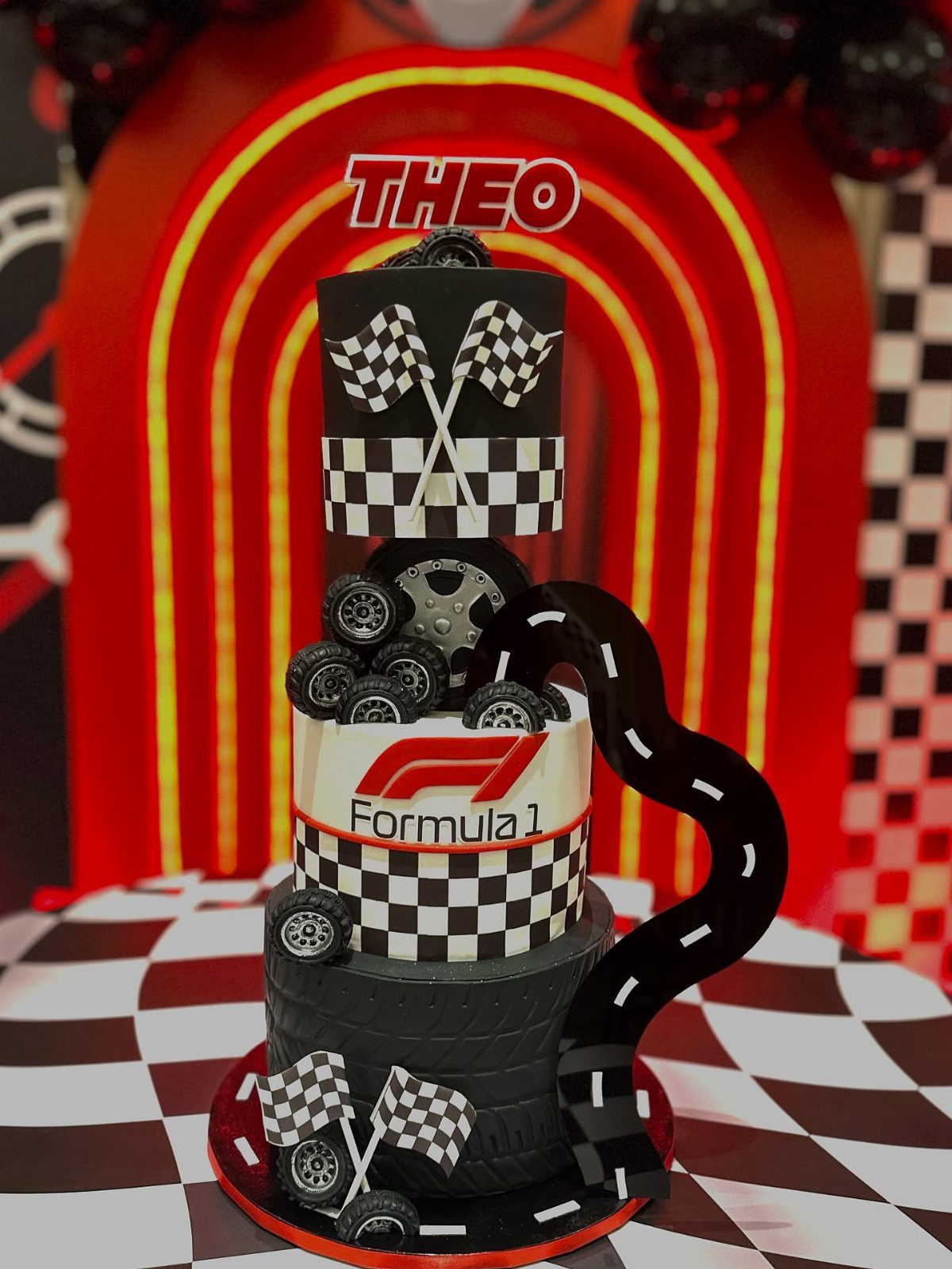 Multi-tiered Formula 1 racing cake with checkered flags, tires, and a black fondant road.