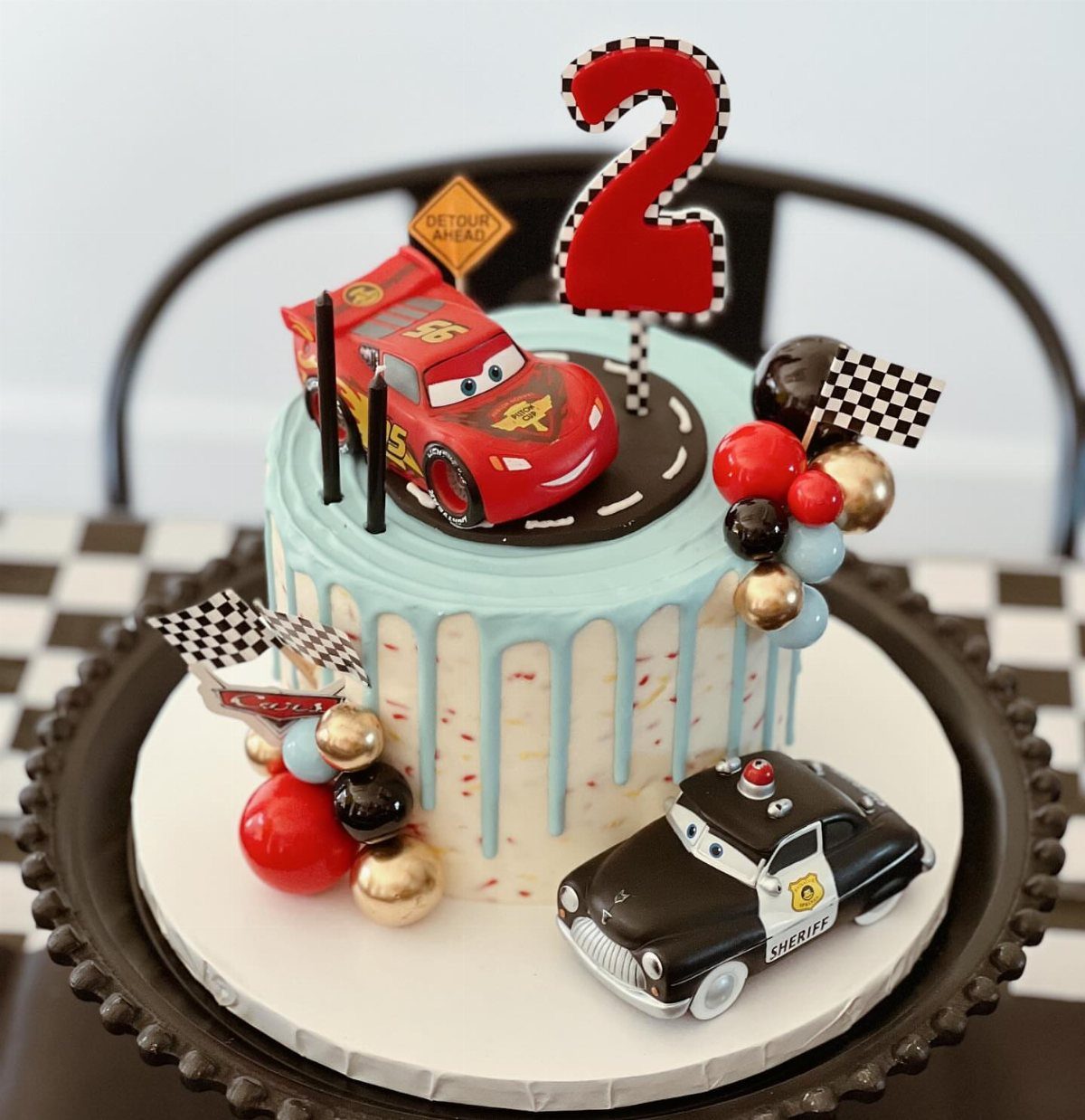 Confetti cake with light blue drip, red race car, and police car decorations.