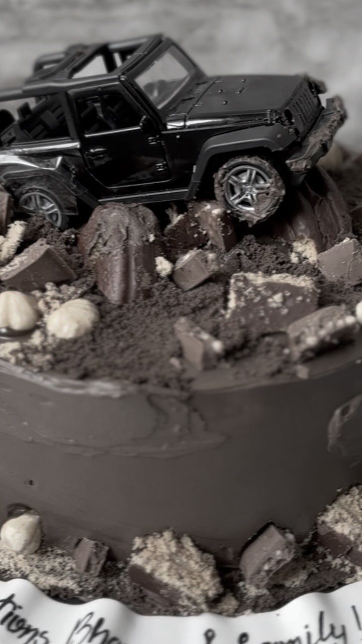 Chocolate cake with a black toy Jeep climbing over chocolate crumbs and chunks.