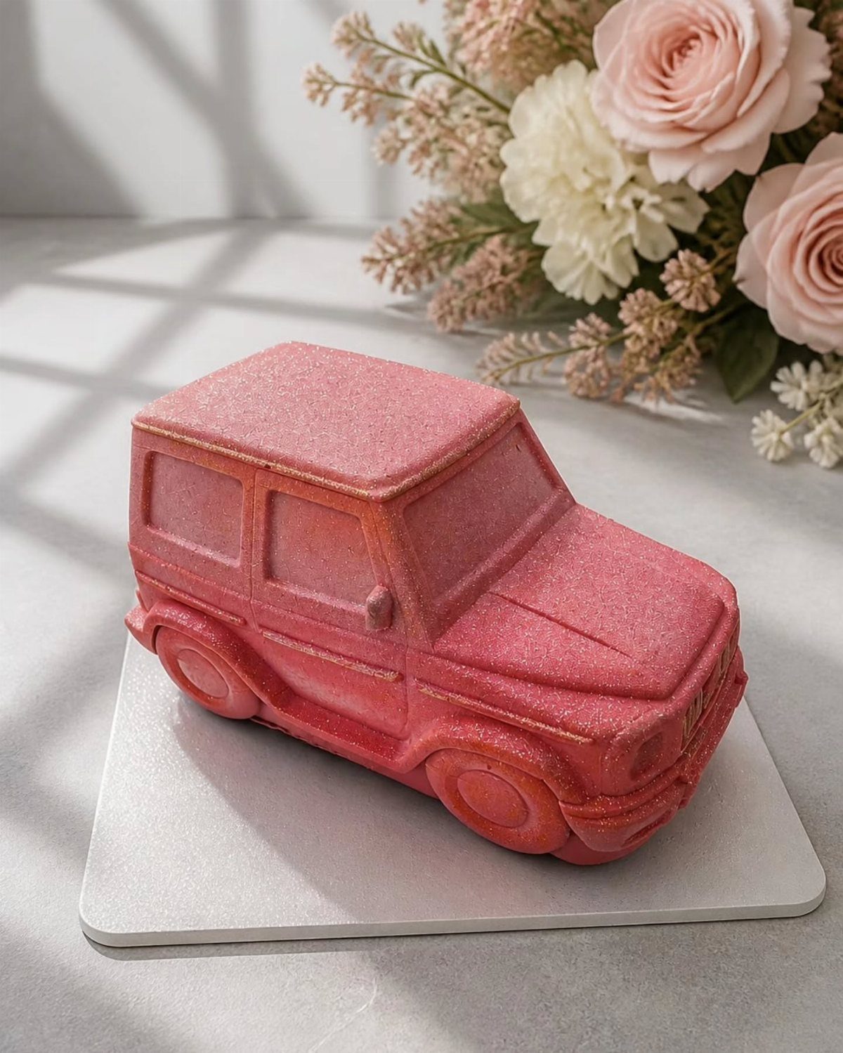 Pink glittery car cake shaped like an SUV next to pink roses