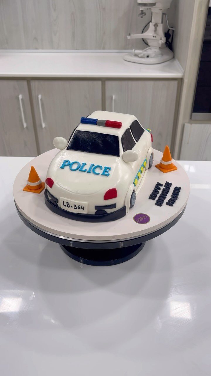 Police car shaped cake with sirens and orange traffic cones on a white base.