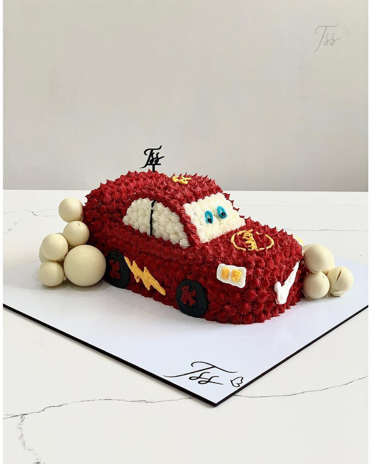 Red car-shaped cake with frosting swirls and yellow lightning bolt on white board.