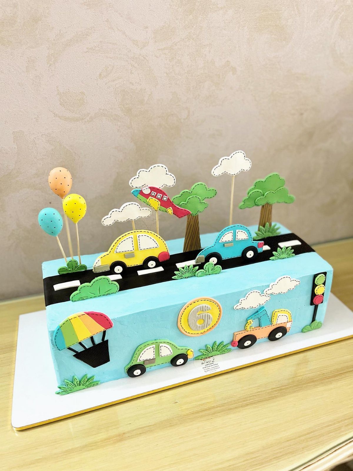 Rectangular blue cake with a road, colorful cars, trees, and balloons on top.