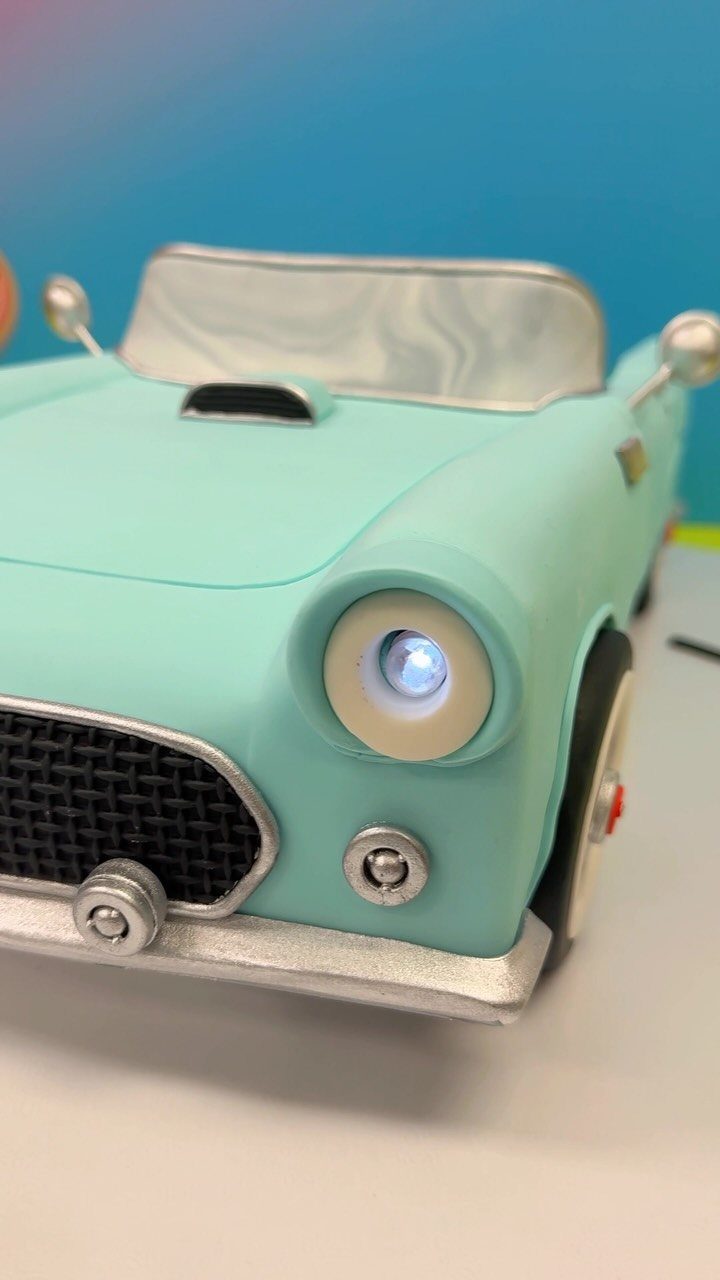 Light blue vintage convertible car cake with a glowing headlight and silver bumpers.
