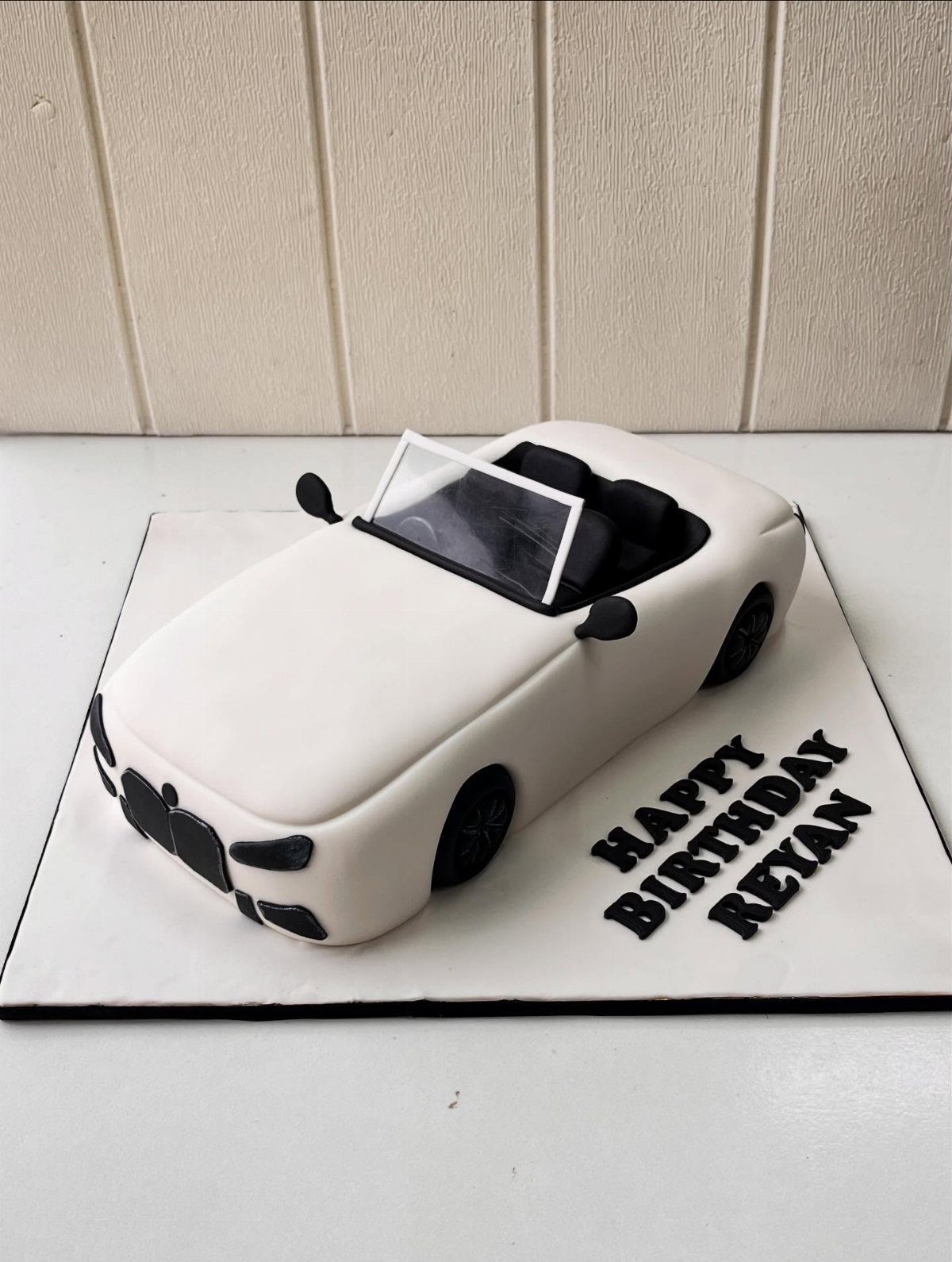 White convertible car cake on a board with Happy Birthday Reyan text.