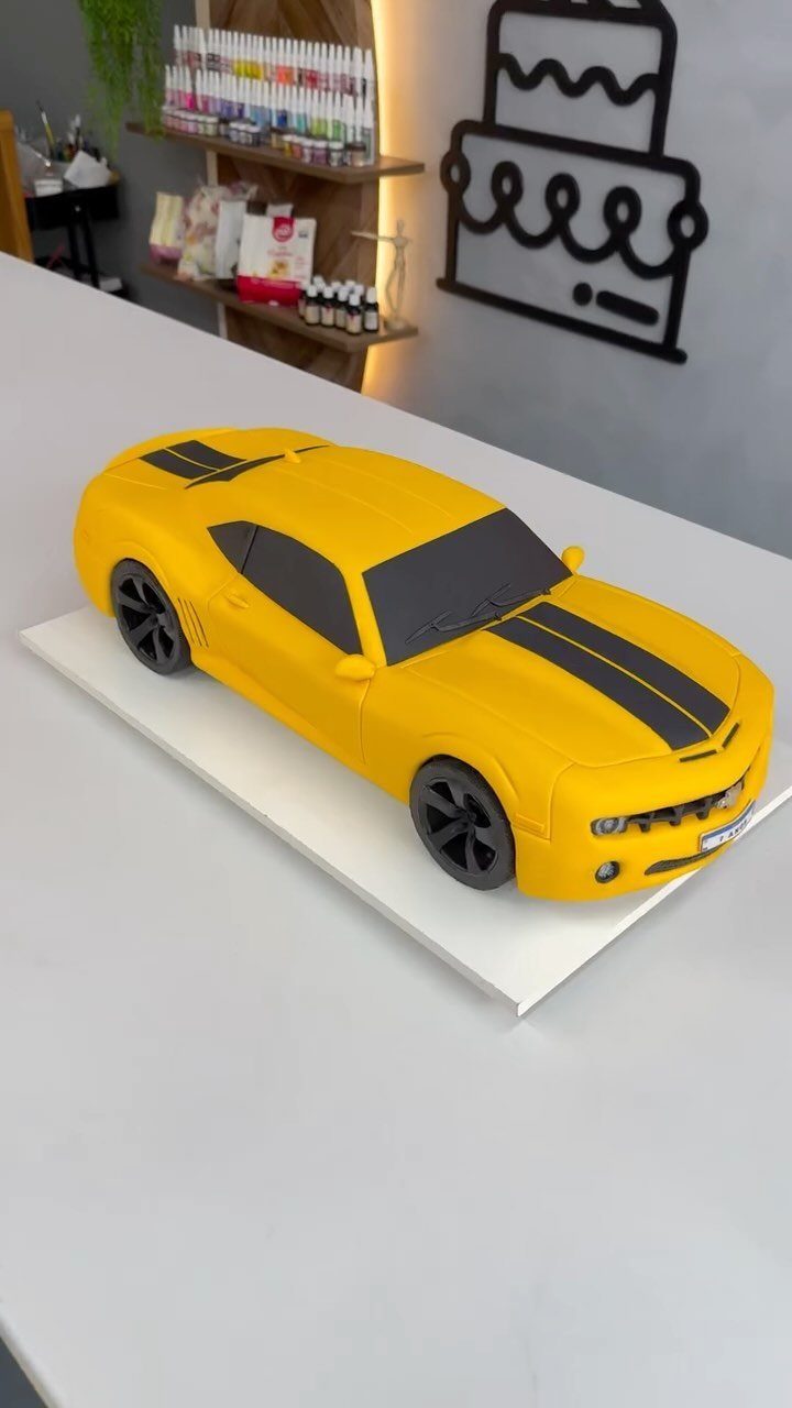 Yellow car cake with black racing stripes on a white display board.