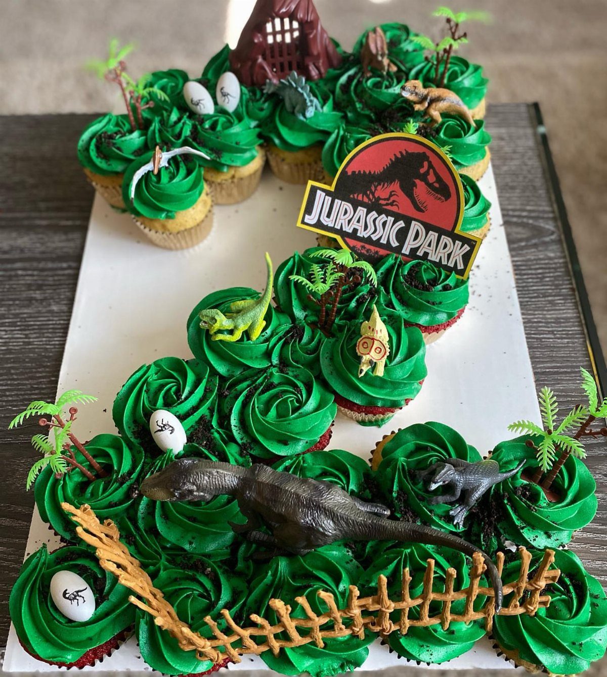 12 Cupcake Cake Ideas for Your Next Celebration 7 Dinosaur themed cupcake cake shaped like a number three with green frosting and figures.