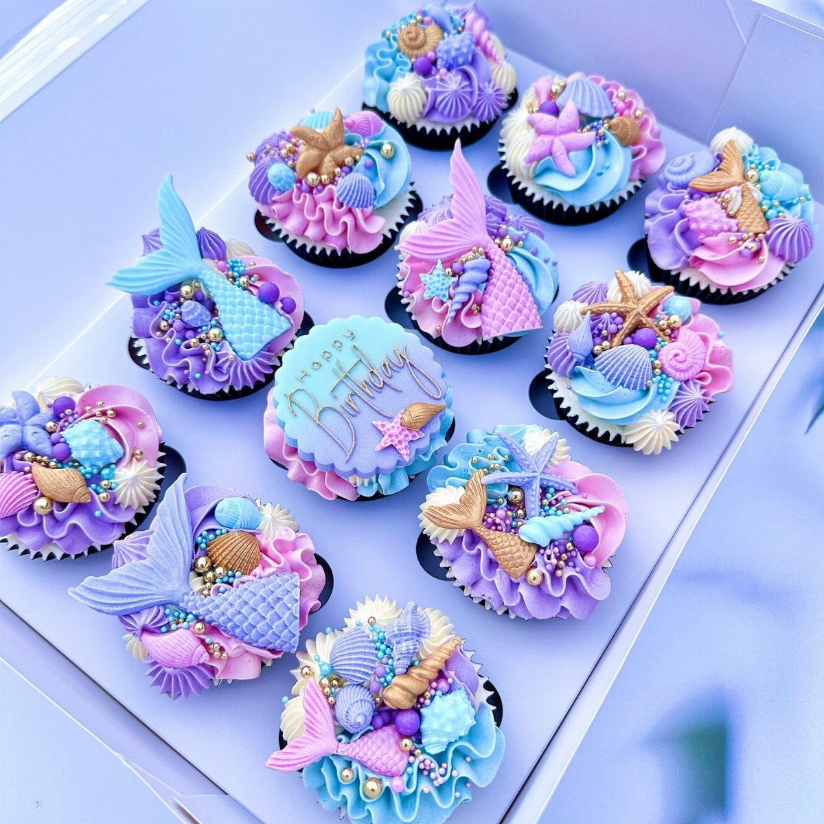 12 Cupcake Cake Ideas for Your Next Celebration 12 Mermaid themed cupcakes with pastel frosting, seashells, and mermaid tails in a box.