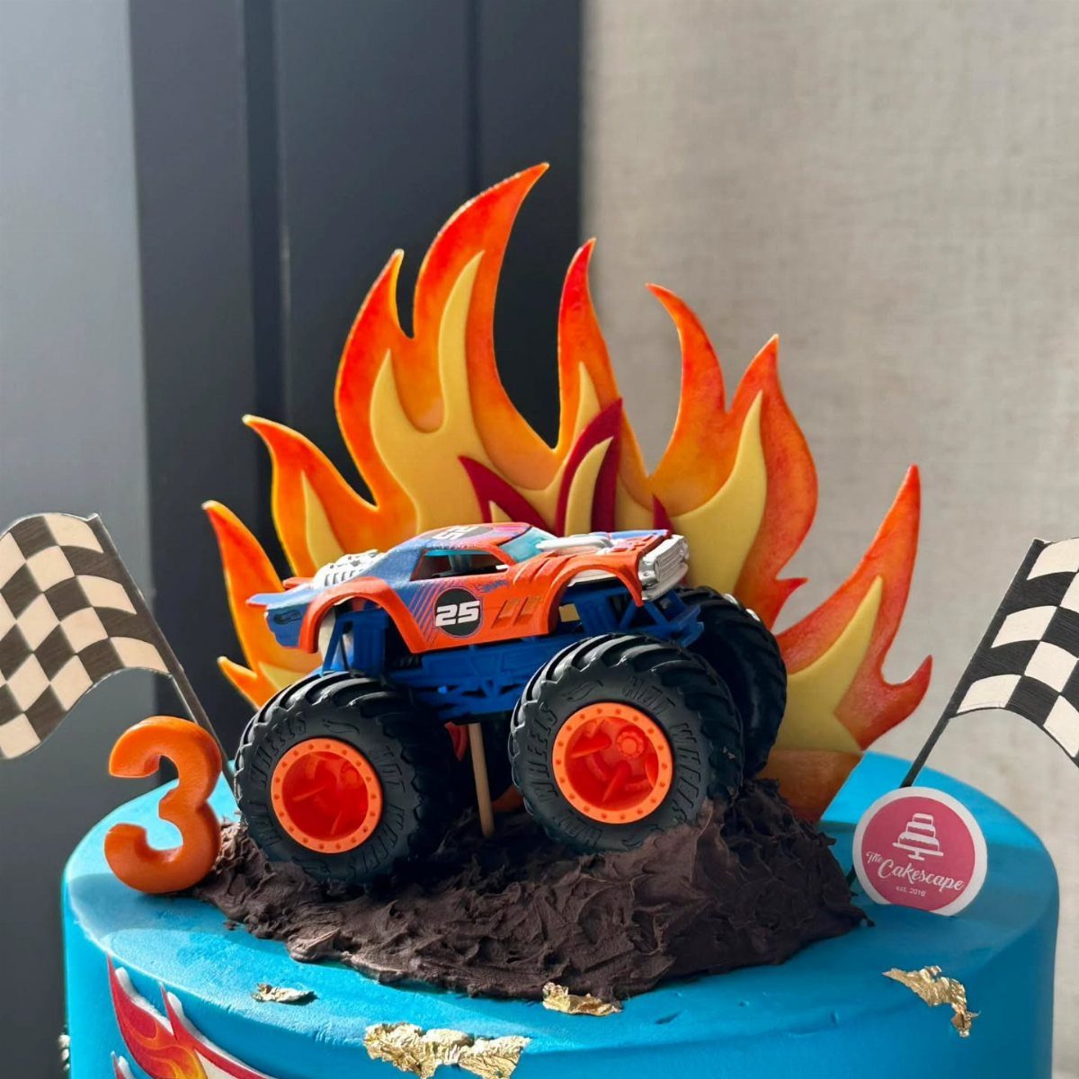 Blue monster truck toy on a chocolate mound atop a blue birthday cake.
