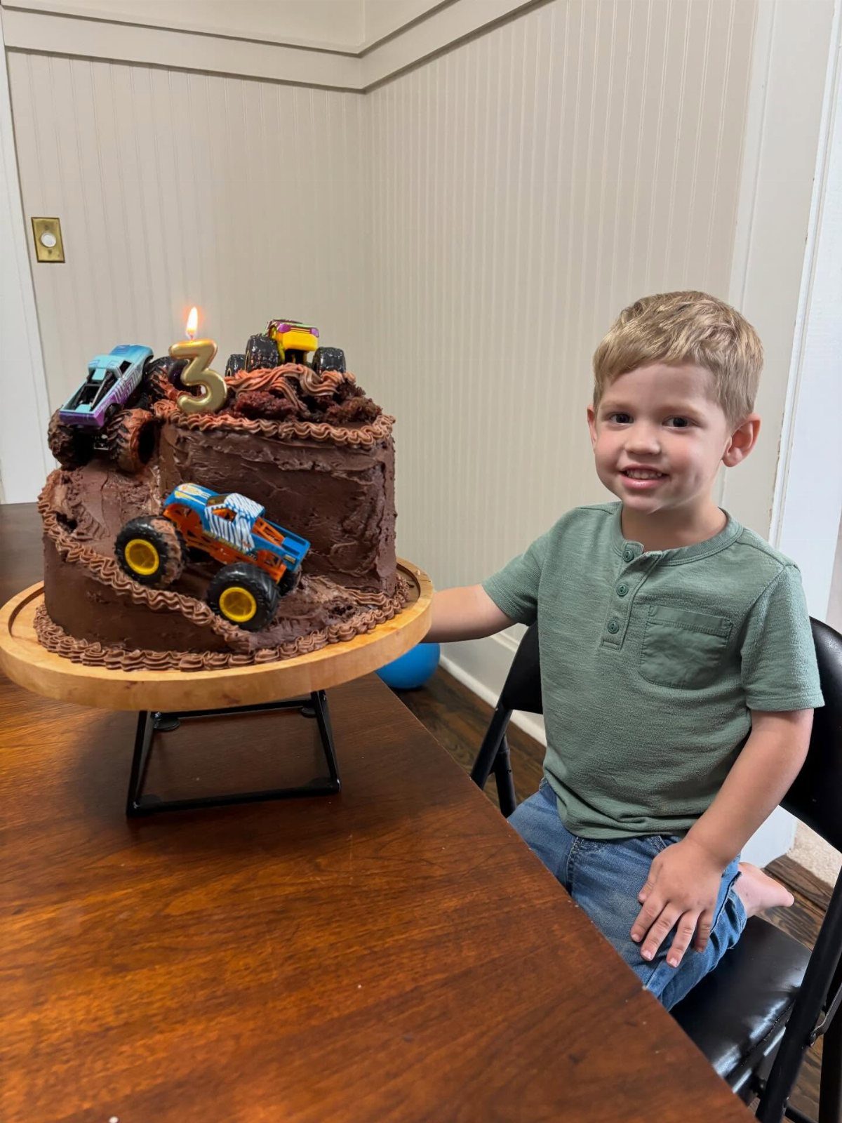 Chocolate monster truck cake with toy trucks and a number 3 candle.