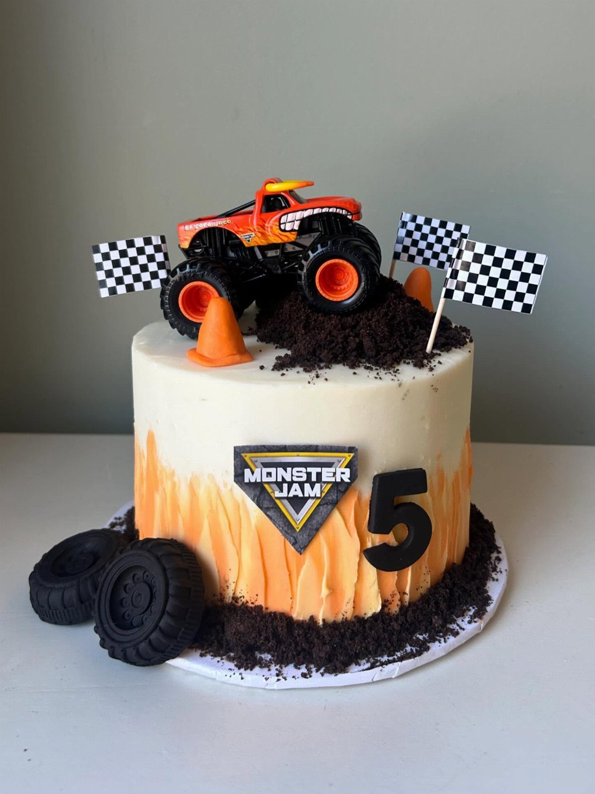 Monster Jam birthday cake with orange toy truck, checkered flags, and chocolate dirt.