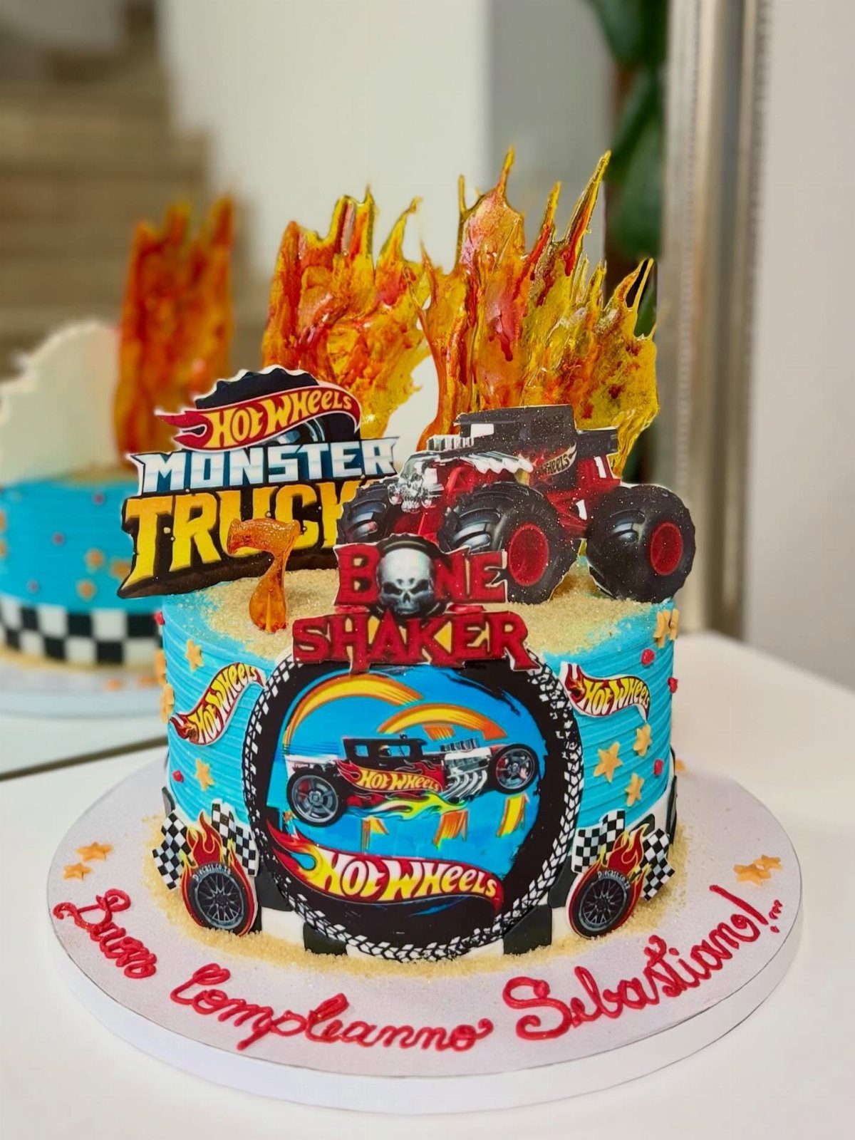 Blue Hot Wheels Bone Shaker birthday cake with toy monster truck and sugar flames.