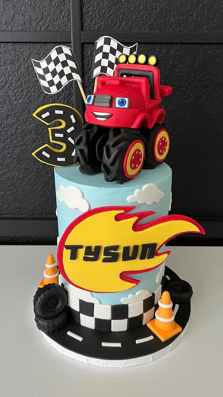 Two-tier blue cake with a red monster truck, checkered flags, and orange traffic cones.