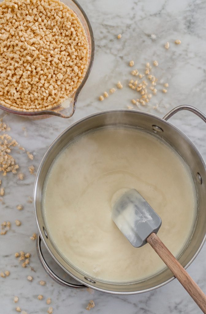 A pot filled with melted marshmallows and Rice Krispies cereal being mixed.