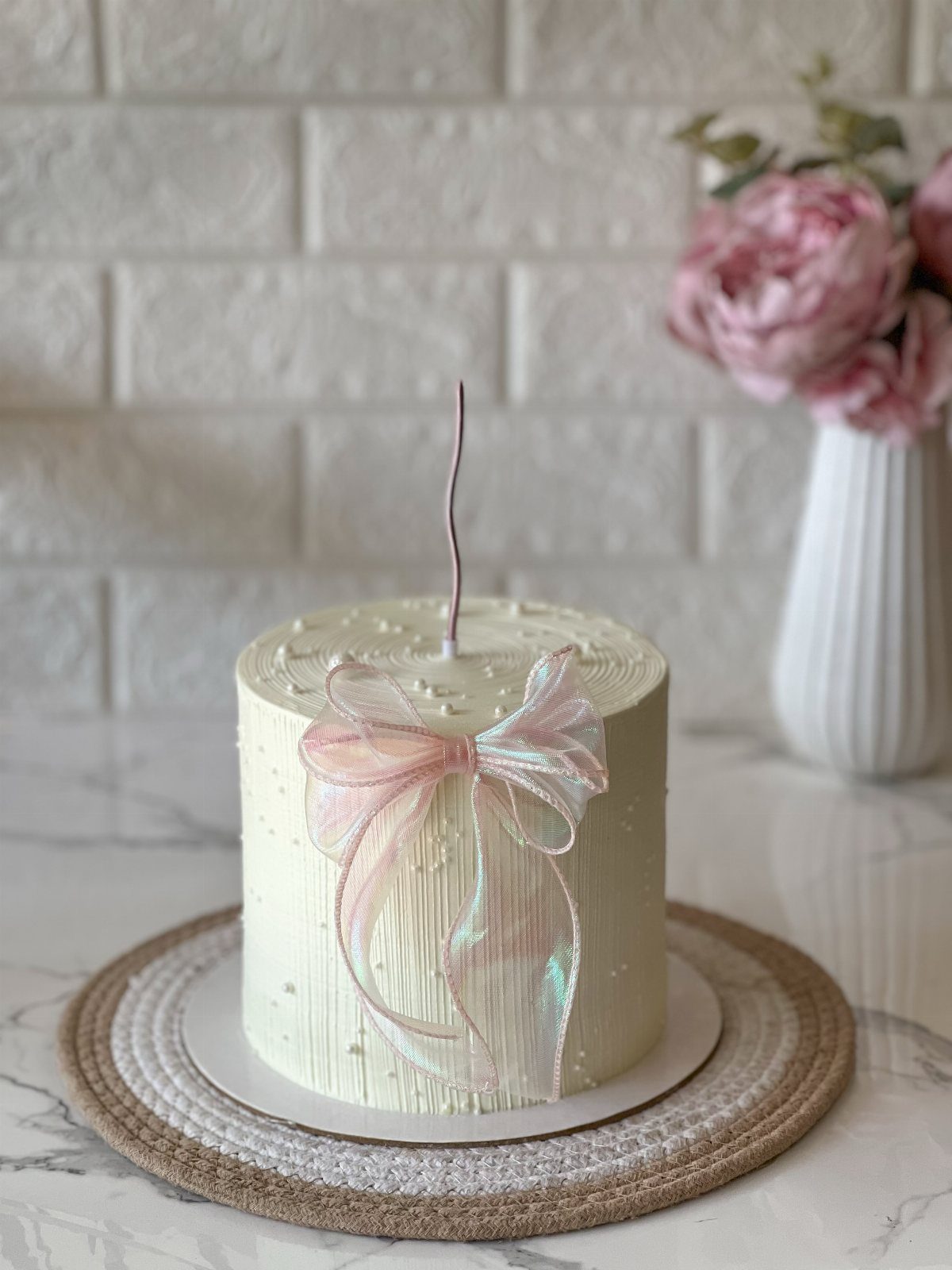 White frosted cake decorated with a large iridescent rose gold ribbon bow.