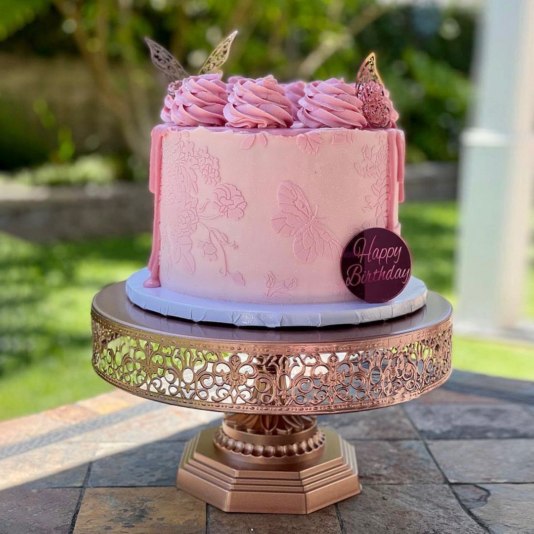 Pink embossed cake with gold butterflies on an ornate rose gold cake stand.