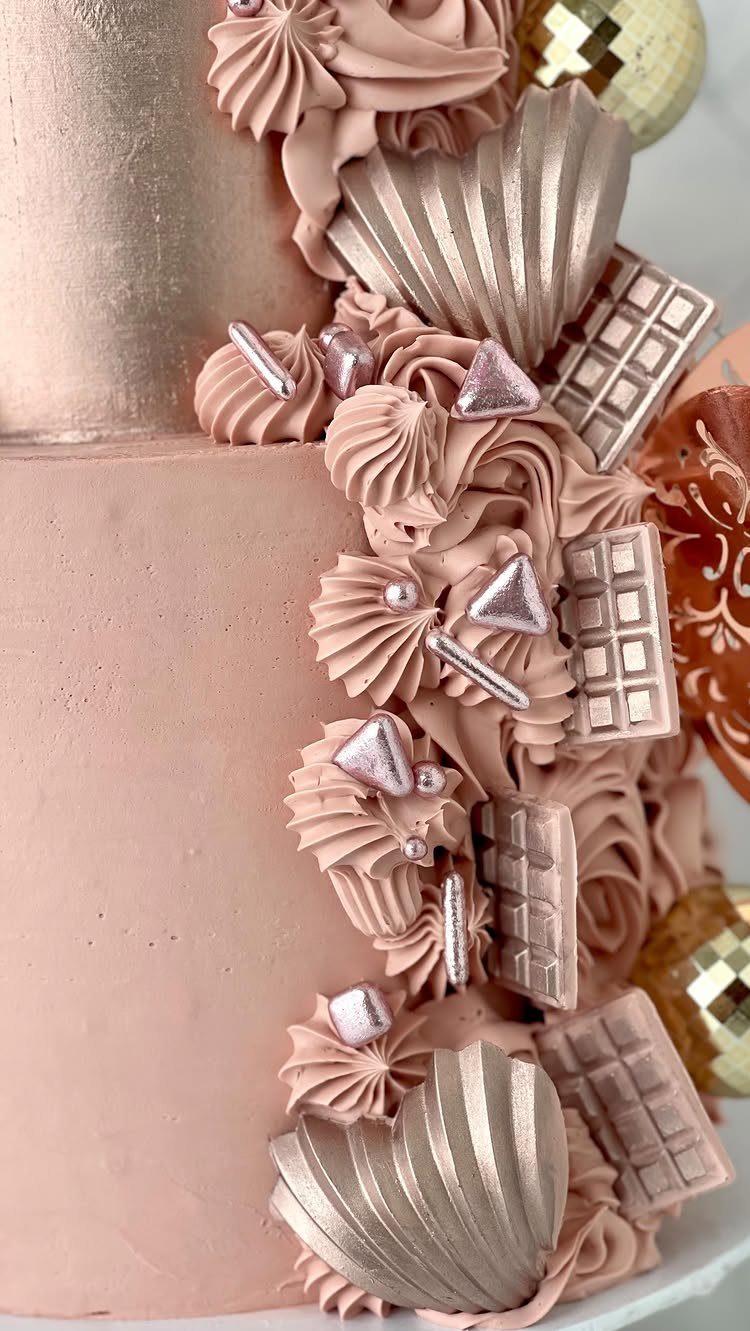 Rose gold cake with metallic pink frosting, chocolate bars, and shell decorations.