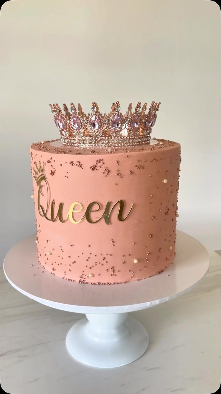 Rose gold cake with a sparkling crown topper and gold Queen script decoration.