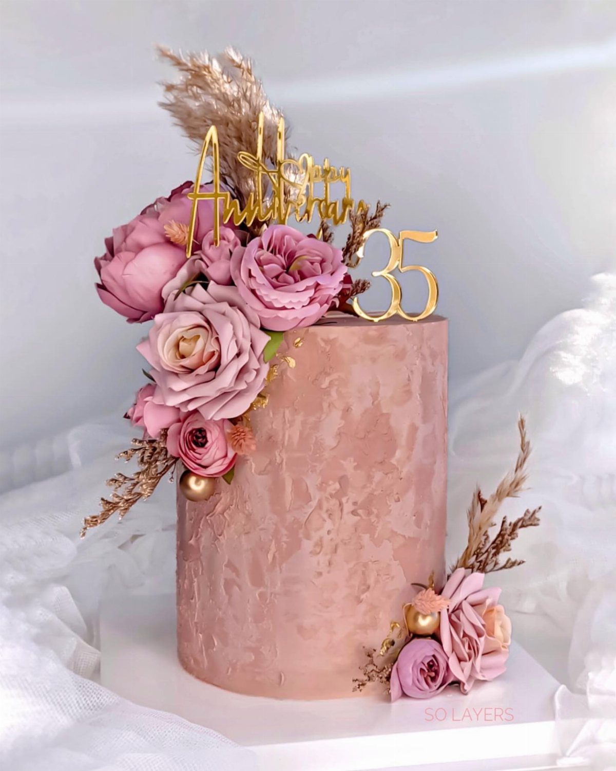 Rose gold textured cake decorated with pink roses, pampas grass, and gold toppers.