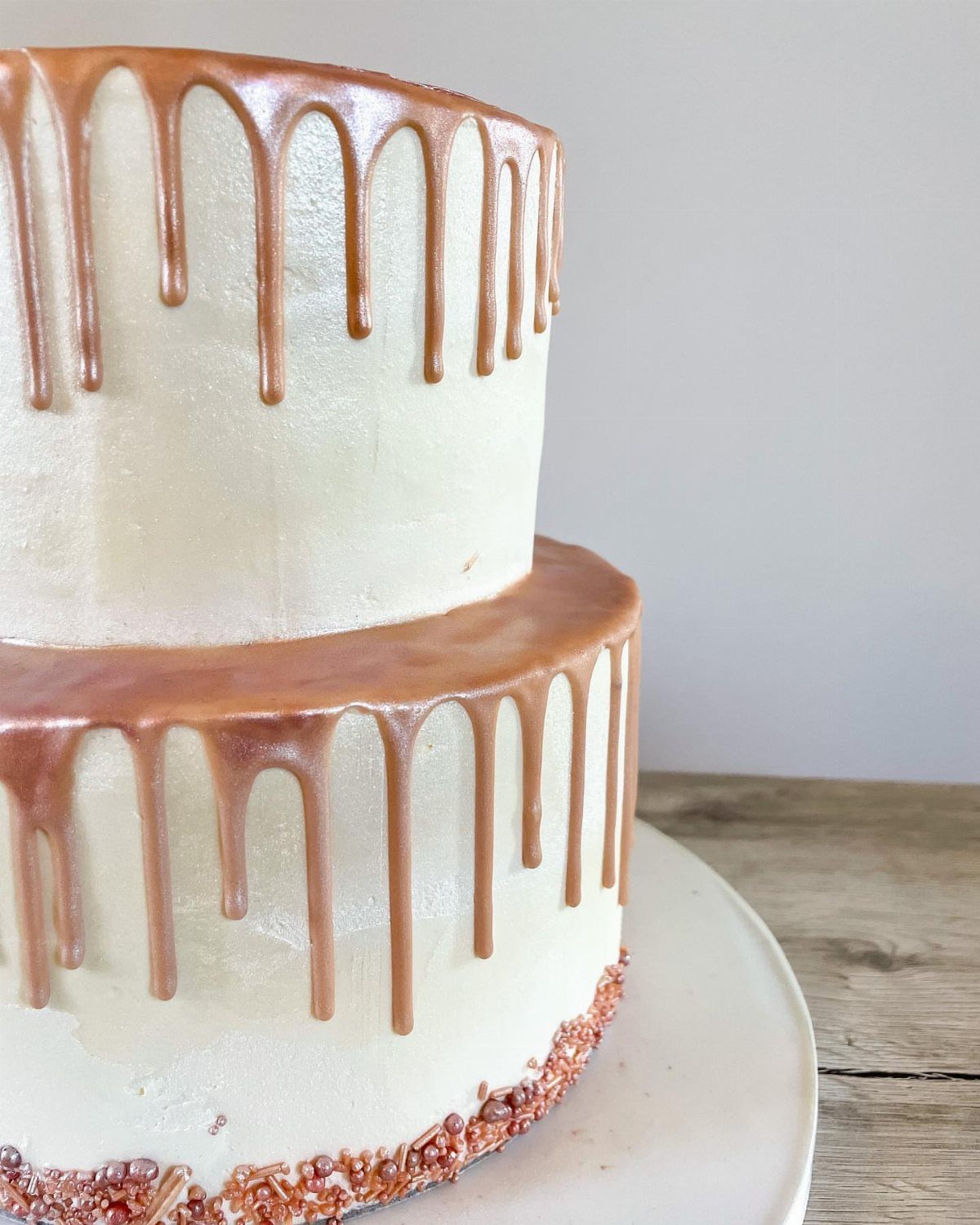 Two-tier white cake with metallic rose gold drip icing and matching sprinkles.
