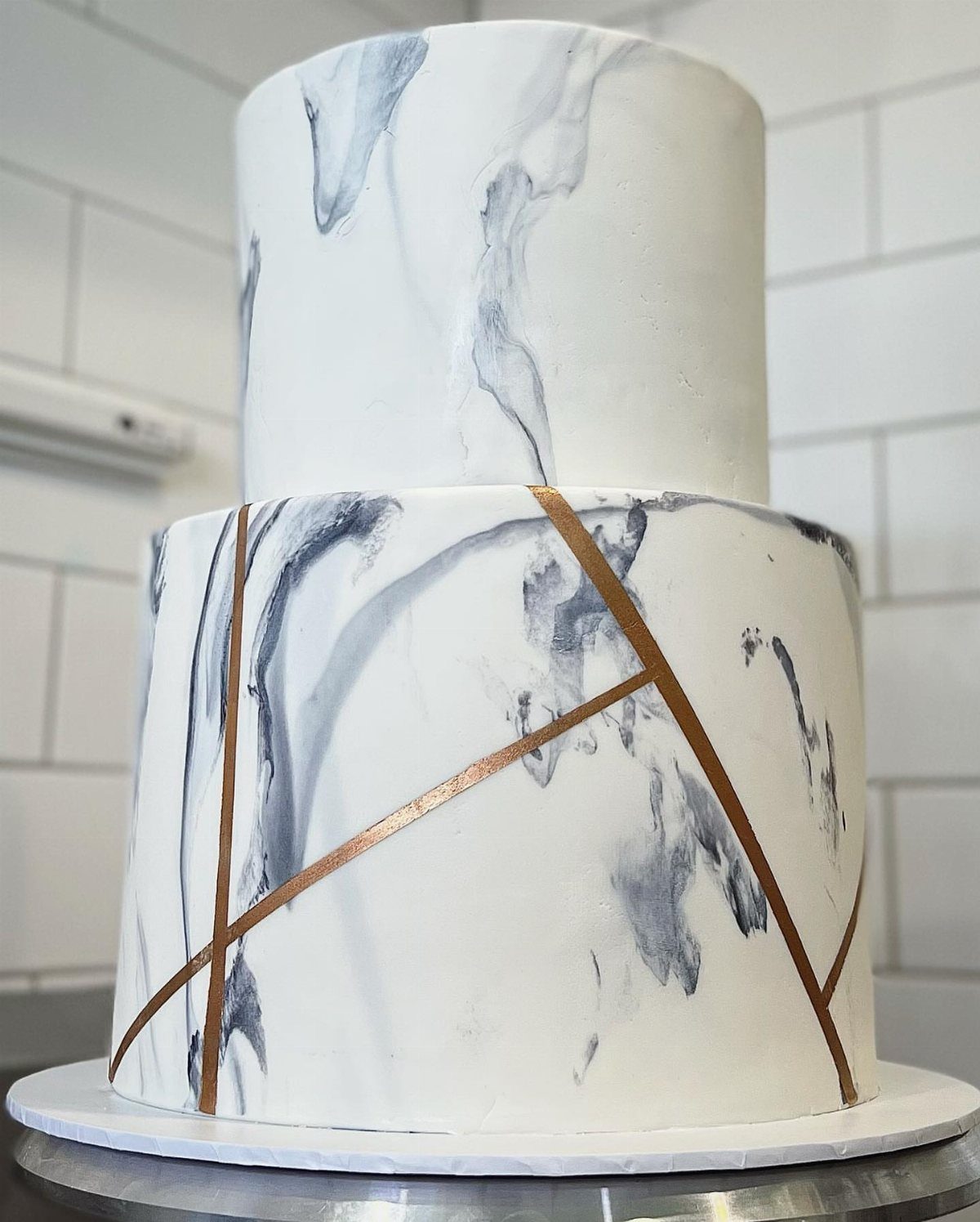 Two-tier white marble cake with rose gold geometric lines on a white base.