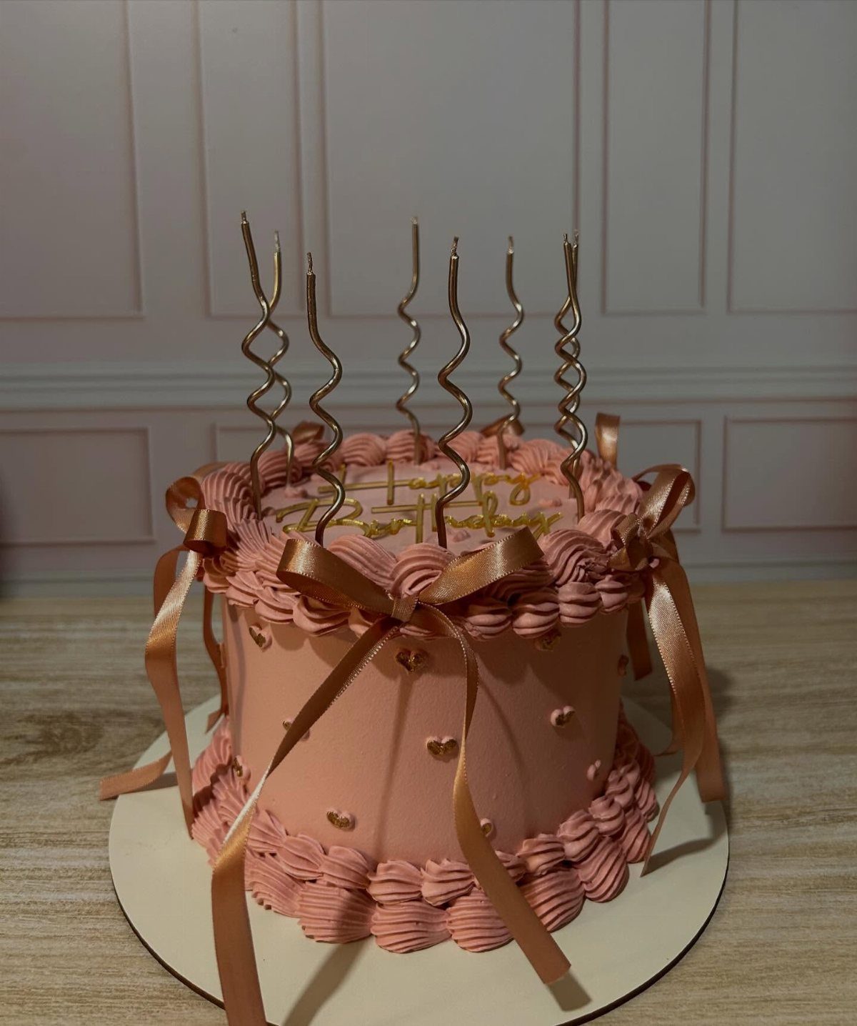 Pink frosted cake with rose gold ribbons and spiral candles on a white background