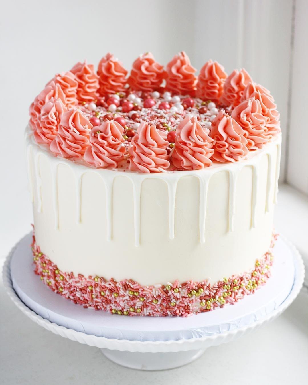 White drip cake with coral frosting swirls and rose gold sprinkle confetti base.