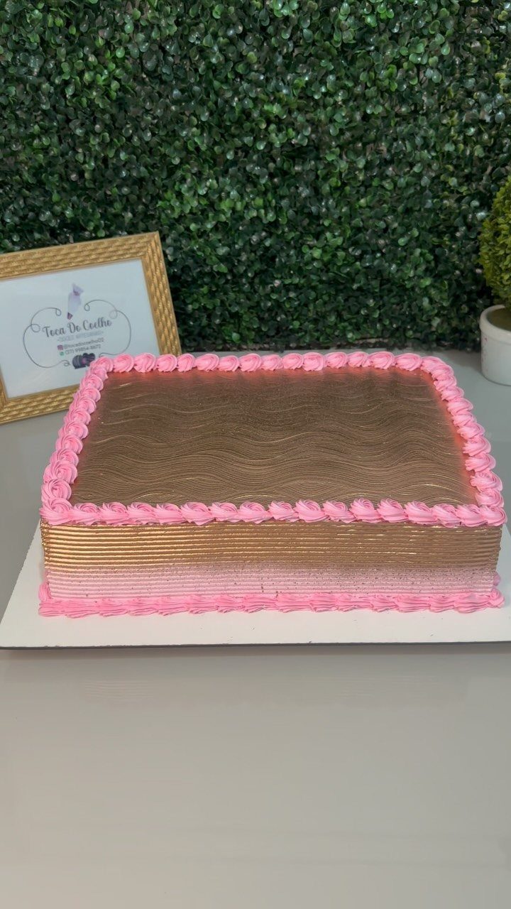 Square rose gold metallic cake with bright pink frosting borders on a white board.