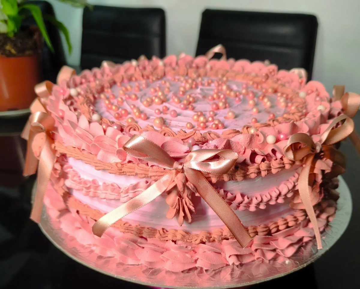 Pink ruffled cake with rose gold ribbons and edible pearls on top.