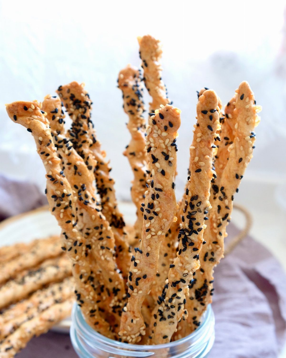 Sourdough Discard Breadsticks with 9 Flavor Ideas 4 Sesame seed breadsticks standing in a glass jar on a light background.