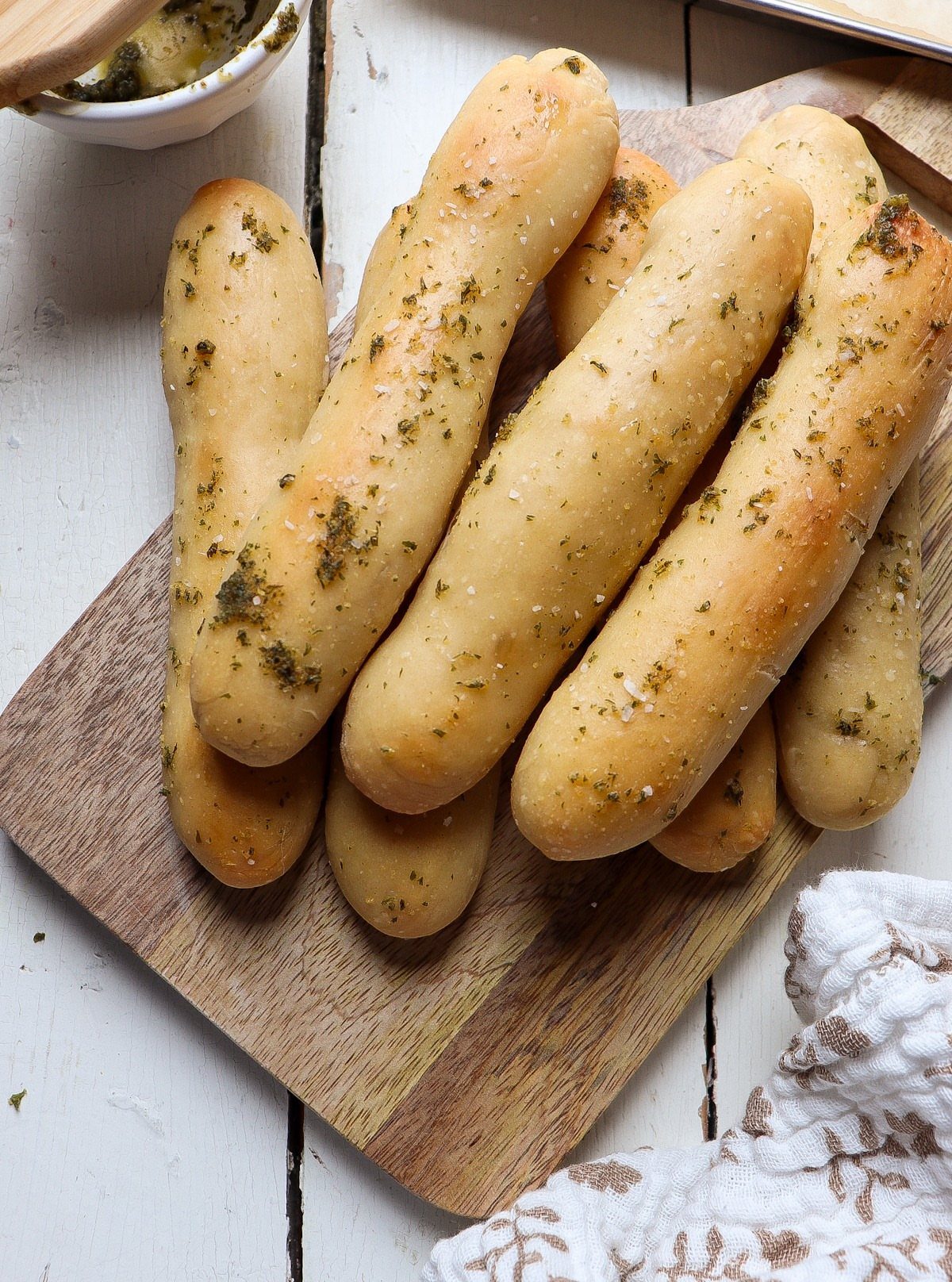 Sourdough Discard Breadsticks with 9 Flavor Ideas 10 Herb-seasoned breadsticks piled on a wooden cutting board with a side of garlic butter.