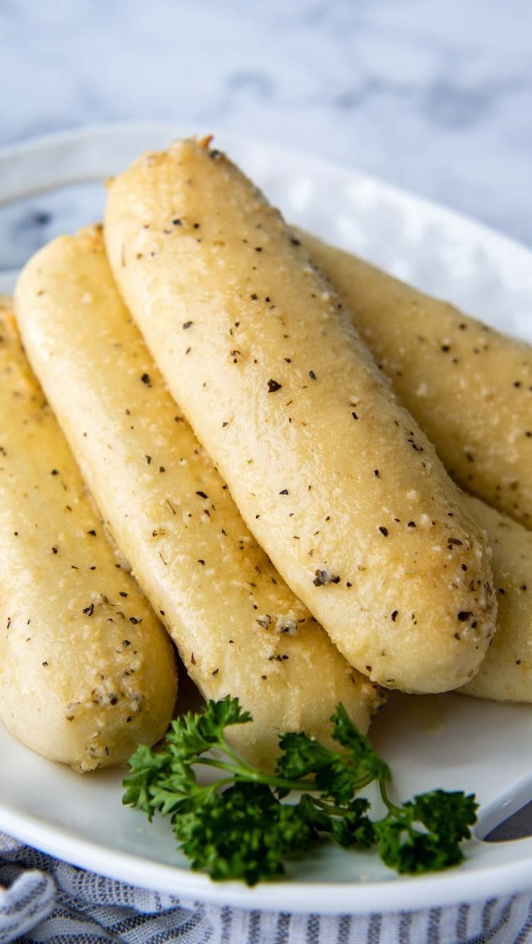 Sourdough Discard Breadsticks with 9 Flavor Ideas 9 Seasoned golden-brown breadsticks on a white plate garnished with a sprig of parsley.