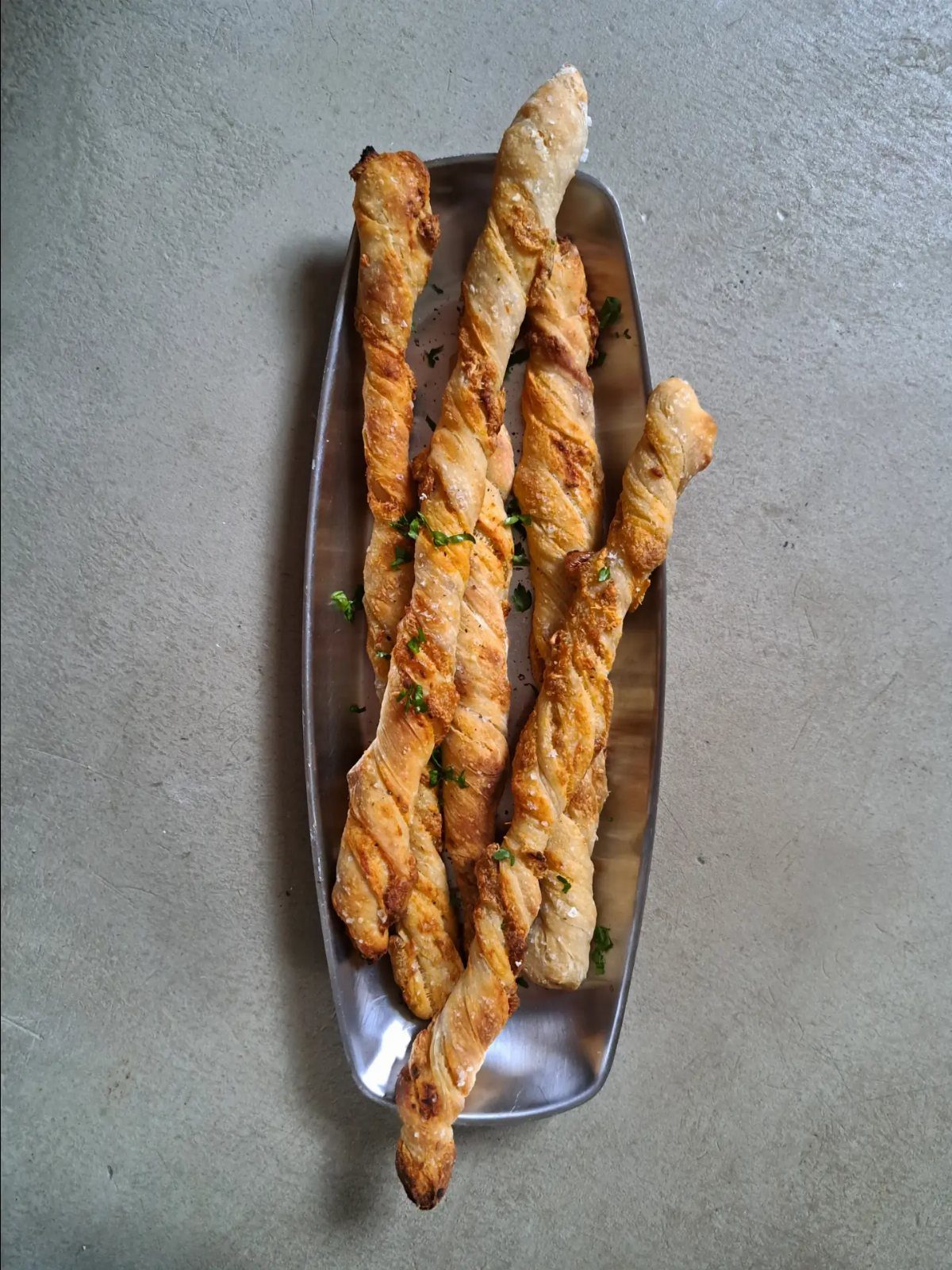 Sourdough Discard Breadsticks with 9 Flavor Ideas 7 Twisted golden-brown breadsticks with green herbs on a silver metal tray.